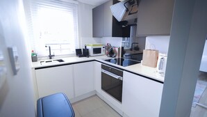A compact kitchen with white cabinets, a microwave, a stove, and a dishwasher. - Camden Serviced Apartments by Globe (London)