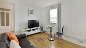 A modern living room with a sofa, a TV, a dining table with chairs, and a window with a city view. - Camden Serviced Apartments by Globe (London)