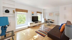 A modern living room with a flat-screen TV, a sofa, a coffee table, and a dining area with a table and chairs. - Camden Serviced Apartments by Globe (London)
