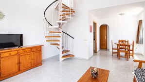 A living room with a wooden TV stand, a spiral staircase, a dining area with wooden chairs, and a patterned sofa. - Al-andalus Casa Azahar (Alcala de Xivert)