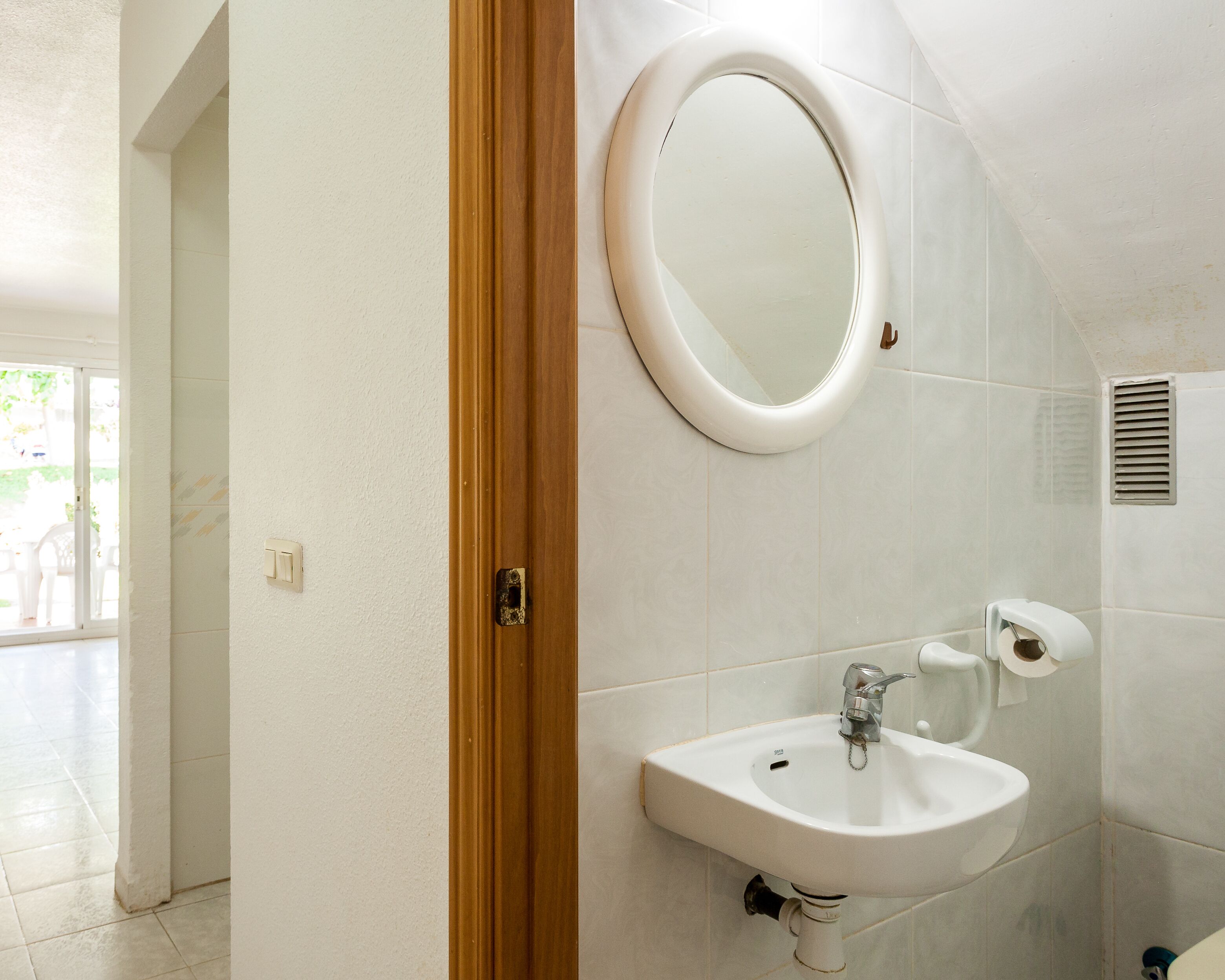 A bathroom with a sink, toilet, and mirror. There is a door leading to another room.