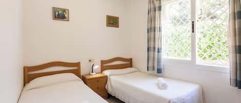 A hotel room with two single beds, a nightstand with a lamp, and a window with curtains.