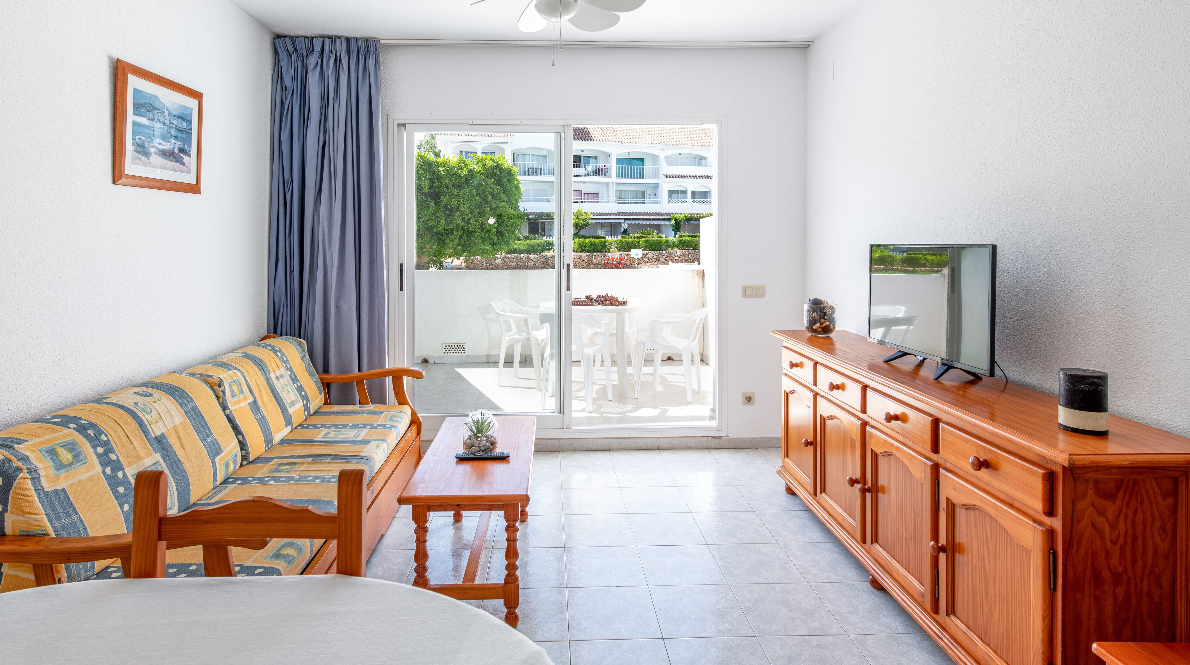 Una sala moderna con un sofá, un mueble de madera, una televisión y vistas a un balcón con mobiliario exterior.