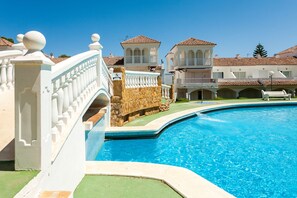 A swimming pool with a stone wall and white balustrade, surrounded by buildings with tiled roofs and balconies. - Al-andalus Casa Azahar (Alcala de Xivert)