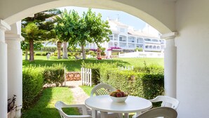 A patio with a white table and chairs, a bowl of fruit, and a view of a well-maintained garden and building in the background. - Al-andalus Casa Azahar (Alcala de Xivert)