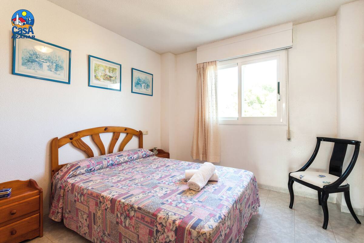 A bedroom with a bed, a chair, and two framed pictures on the wall.