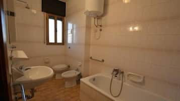 Un baño con una bañera, dos inodoros y un lavabo.