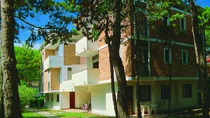 A multi-story building with a brick facade, multiple balconies, and a small courtyard with trees. - Lignano Pineta (Lignano Sabbiadoro)