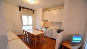 A compact living space with a dining area, kitchenette, and a television on a wooden stand. - Lignano Pineta (Lignano Sabbiadoro)
