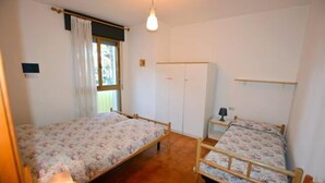 A bedroom with two single beds, a wardrobe, a bedside table with a lamp, and a window with curtains. - Lignano Pineta (Lignano Sabbiadoro)