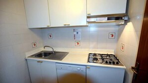 A compact kitchen with white cabinets, a stainless steel sink, a dishwasher, and a gas stove. - Lignano Pineta (Lignano Sabbiadoro)
