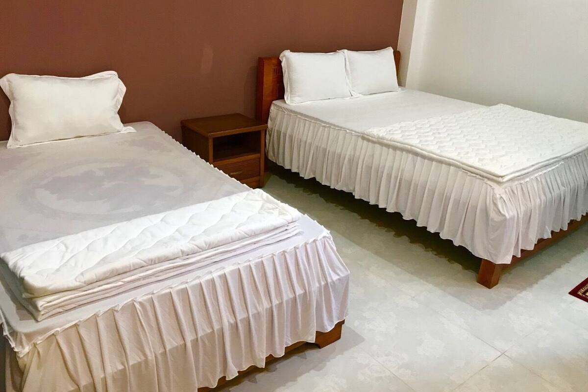 Two single beds with white bedding, a wooden nightstand, and a plain wall.