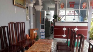 A hotel reception area with a reception desk, chairs, and a long wooden table. - IQ Hotel (Ho Chi Minh City)
