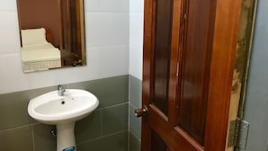 A bathroom with a white pedestal sink, a mirror, and a wooden door. - IQ Hotel (Ho Chi Minh City)