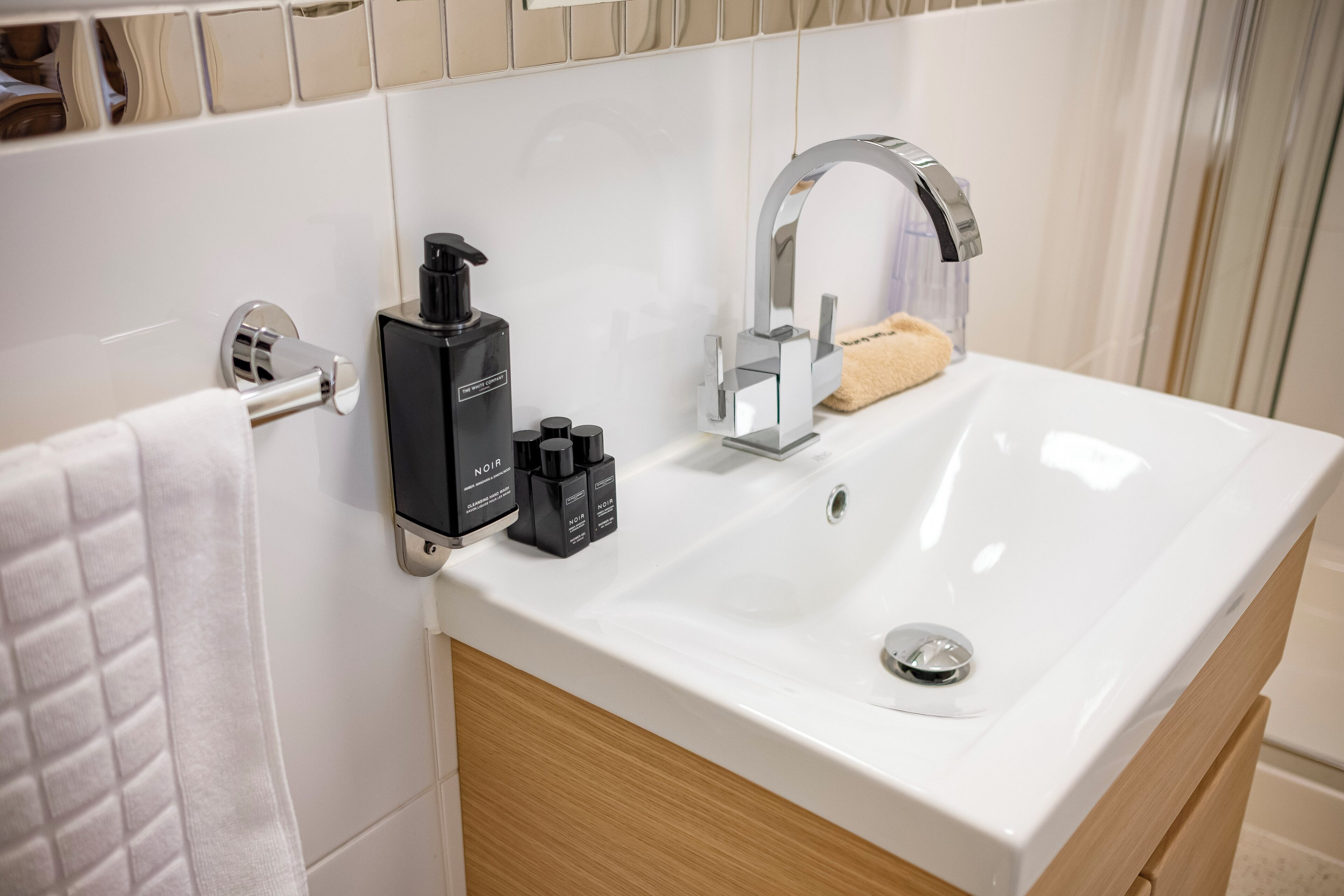 Uma casa de banho moderna com lavatório branco, um porta-toalhas, dispensador de sabonete e espelho.