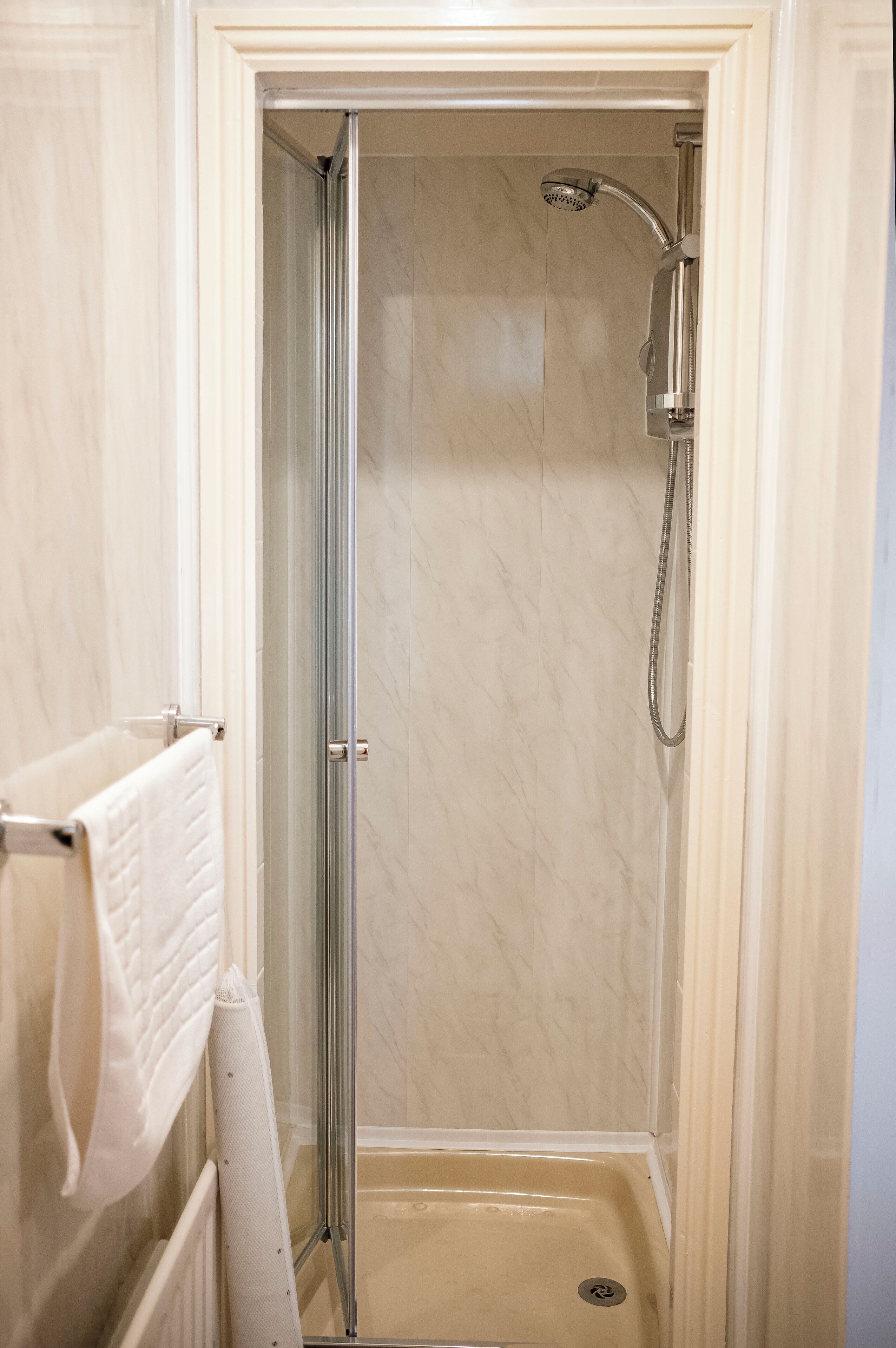 Eine begehbare Dusche mit Glastür, Handtuchhalter und Duschkopf.