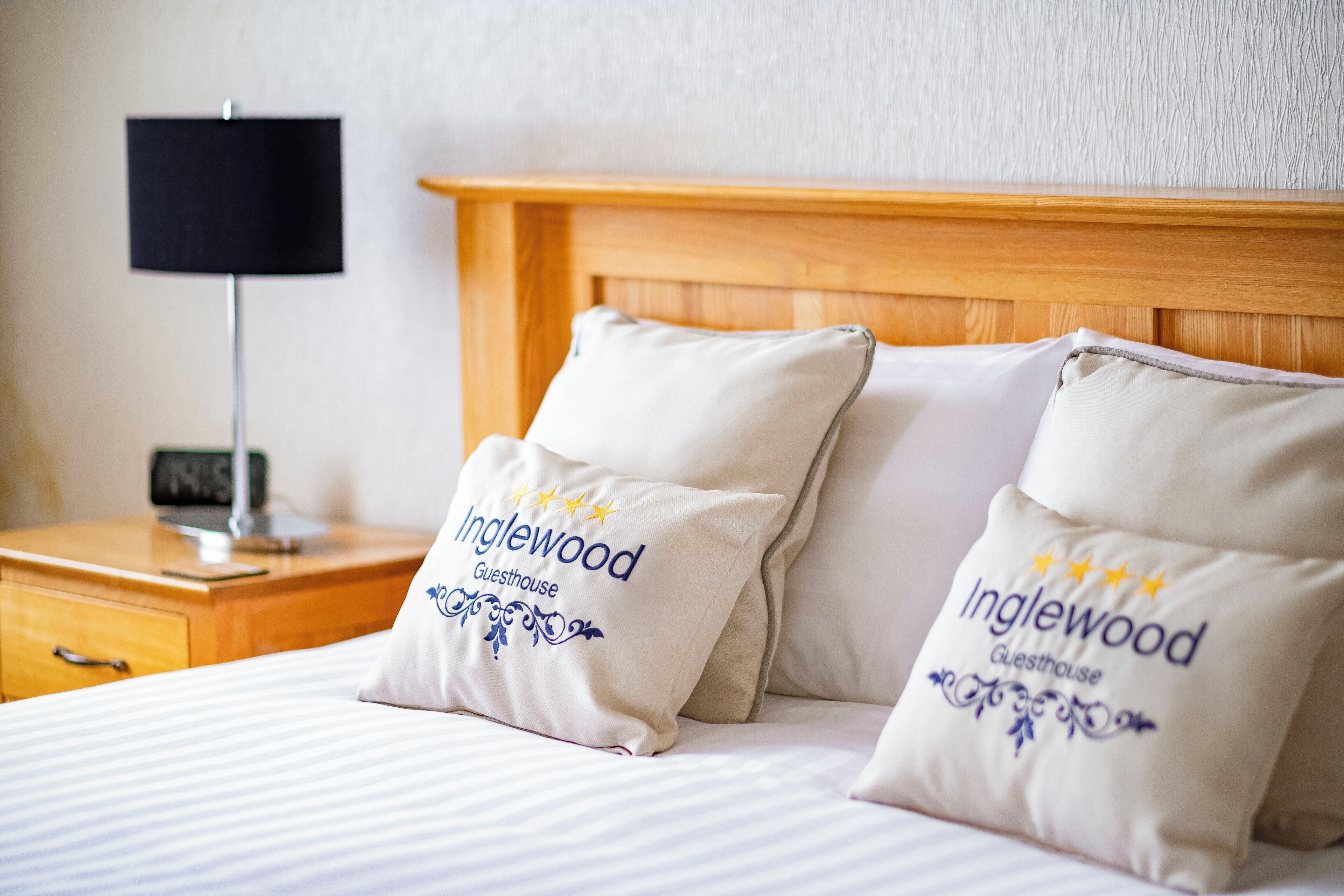 A neatly made bed with two pillows labeled "Inglewood Guesthouse."