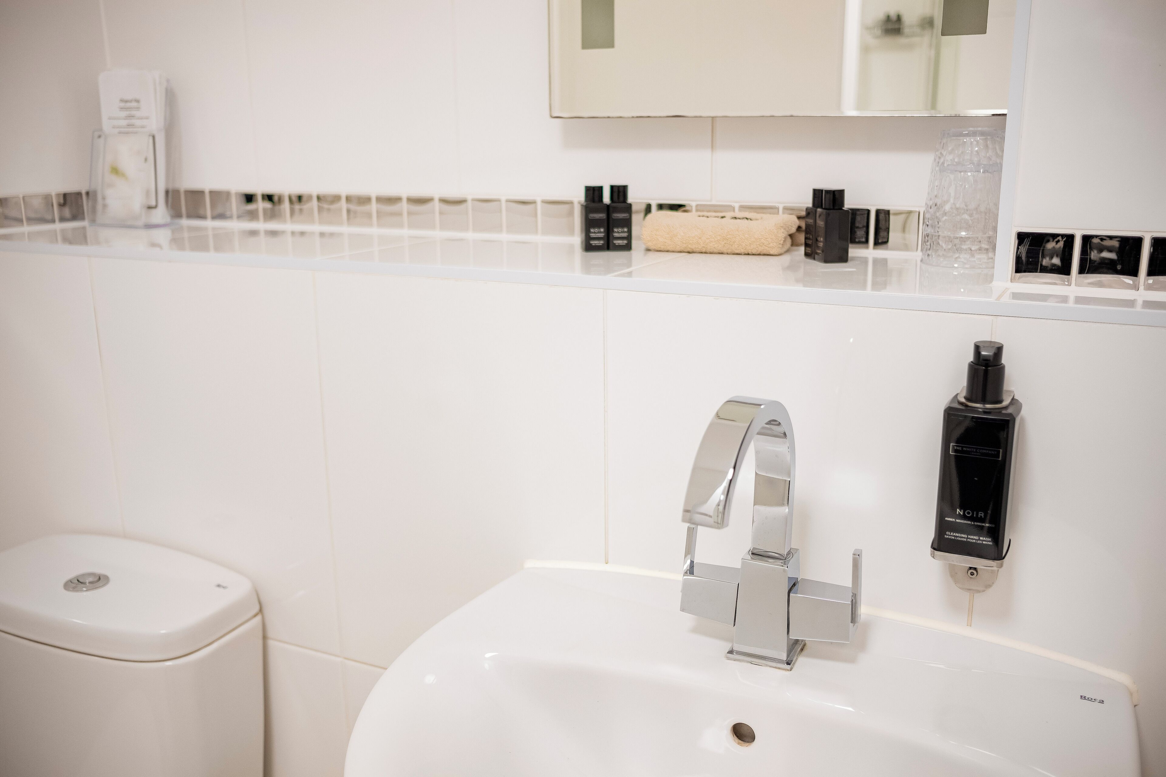 A bathroom with a white sink, chrome faucet, and toiletries on the counter.