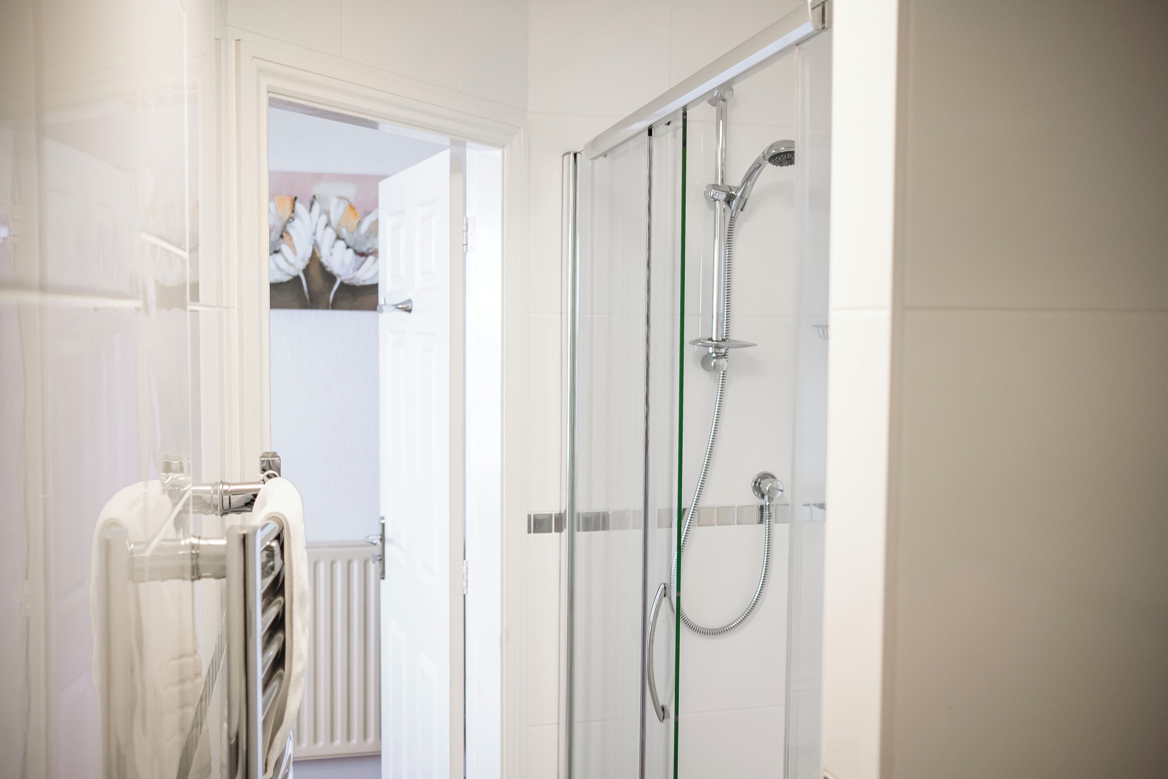 Un baño moderno con cabina de ducha de vidrio, radiador blanco y perchero.