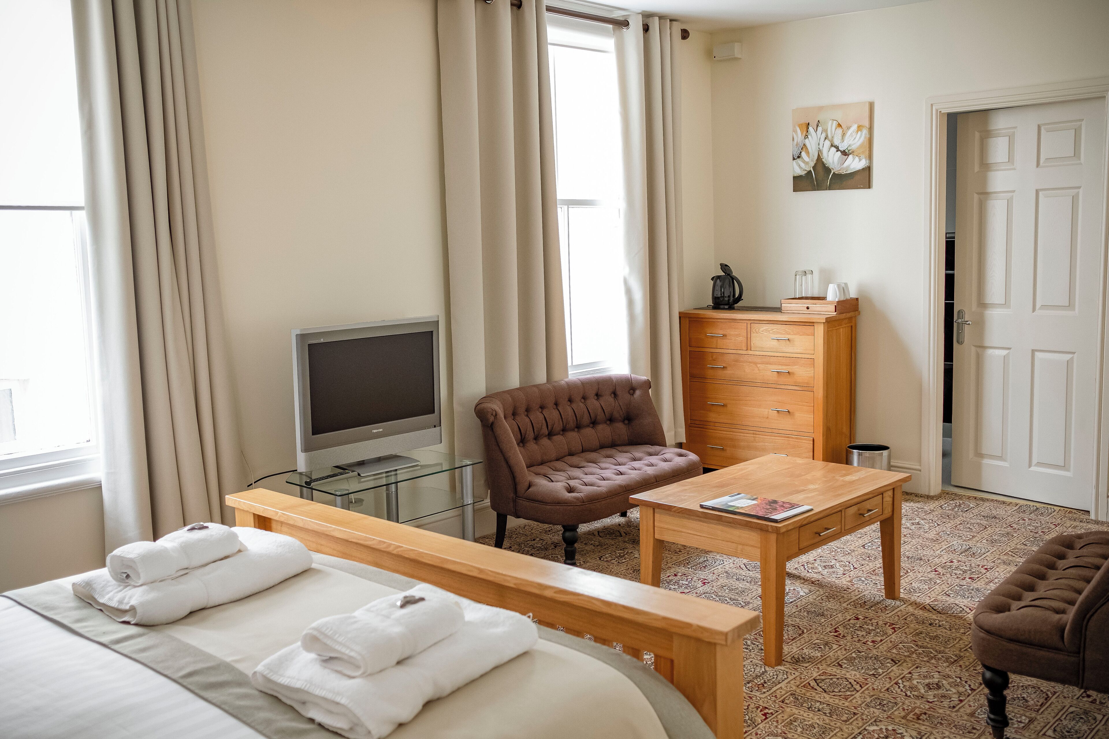 A hotel room with a bed, a TV, a brown armchair, a wooden dresser, and a small table.