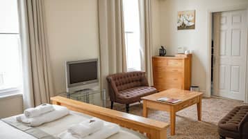 A hotel room with a bed, a TV, a brown armchair, a wooden dresser, and a small table.