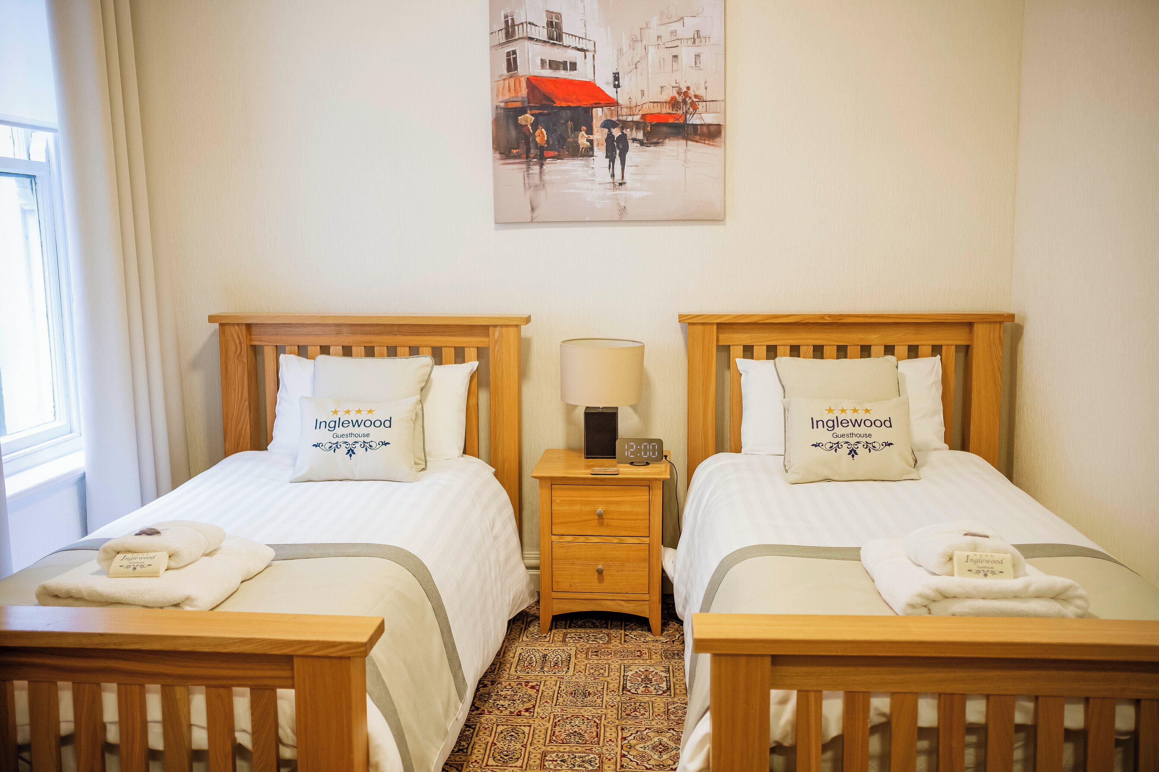 Quarto de hotel com duas camas, uma mesa de cabeceira com abajur e um quadro na parede.