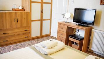 Un dormitorio con cama, armario de madera, televisor y una pequeña mesa de escritorio con espejo.