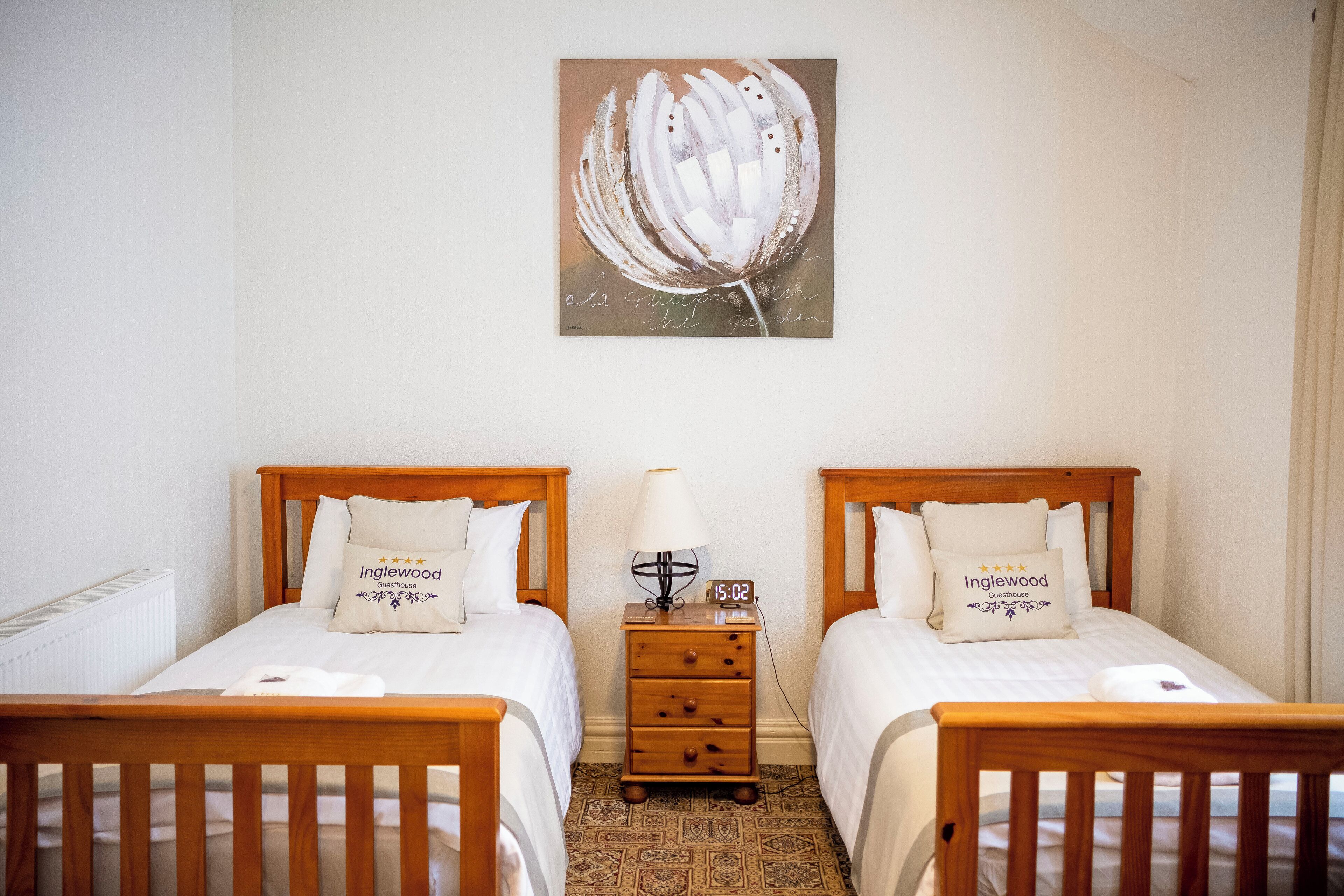 A hotel room with two single beds, a nightstand with a lamp, and a wall-mounted painting.