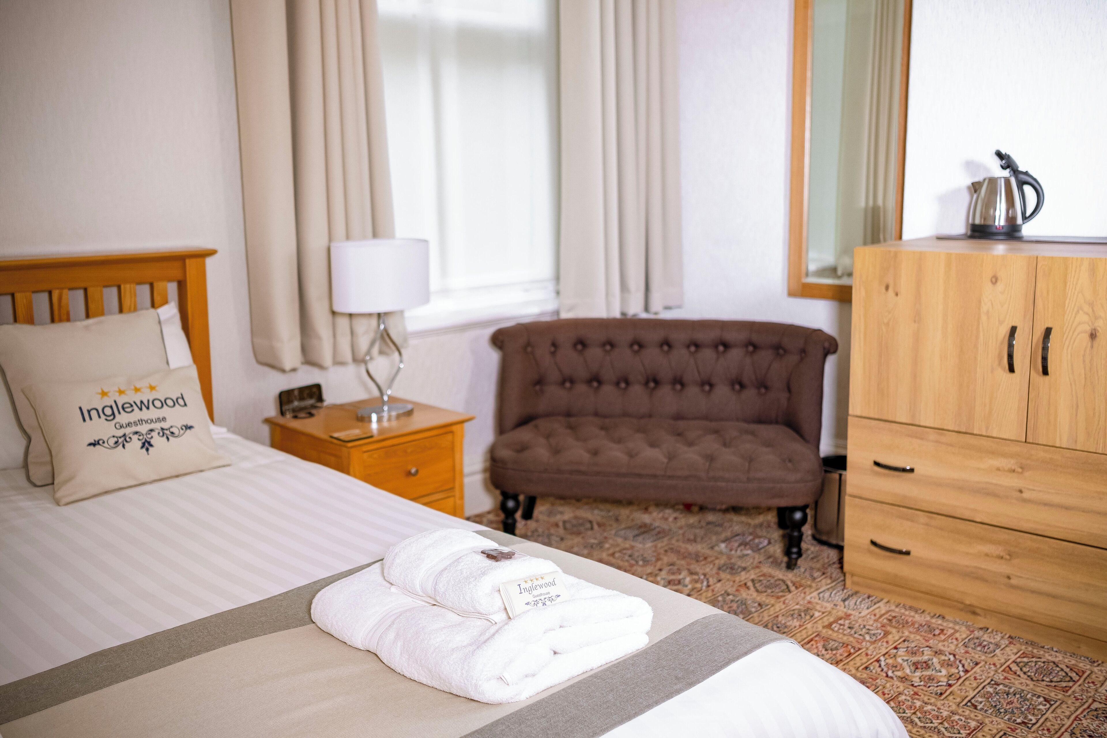 Een hotelkamer met een opgemaakt bed, een bruine gestofte bank, een houten kast en een raam met gordijnen.