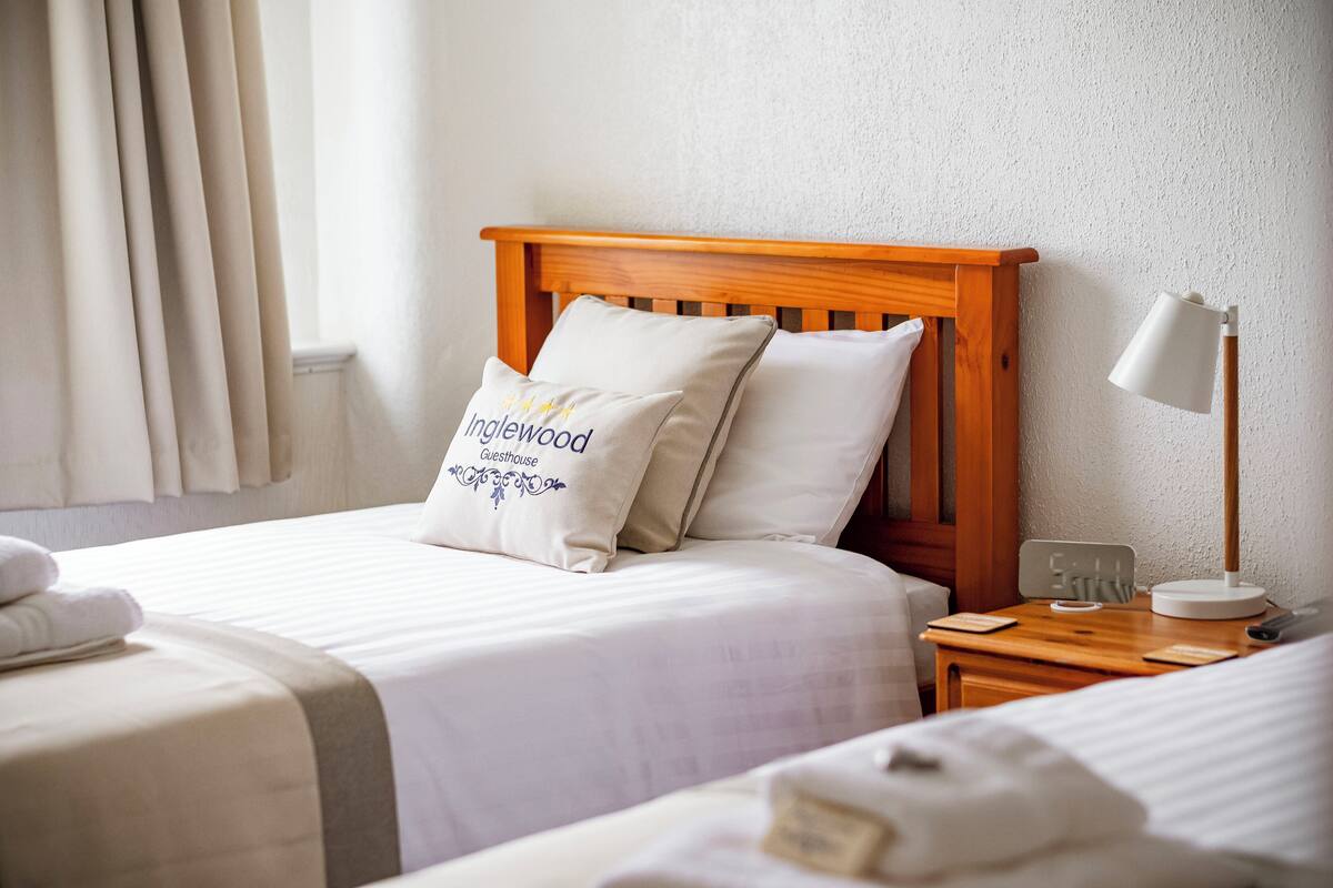 A hotel room with a wooden headboard, two pillows with text, a bedside table with a lamp, and a neatly made bed.