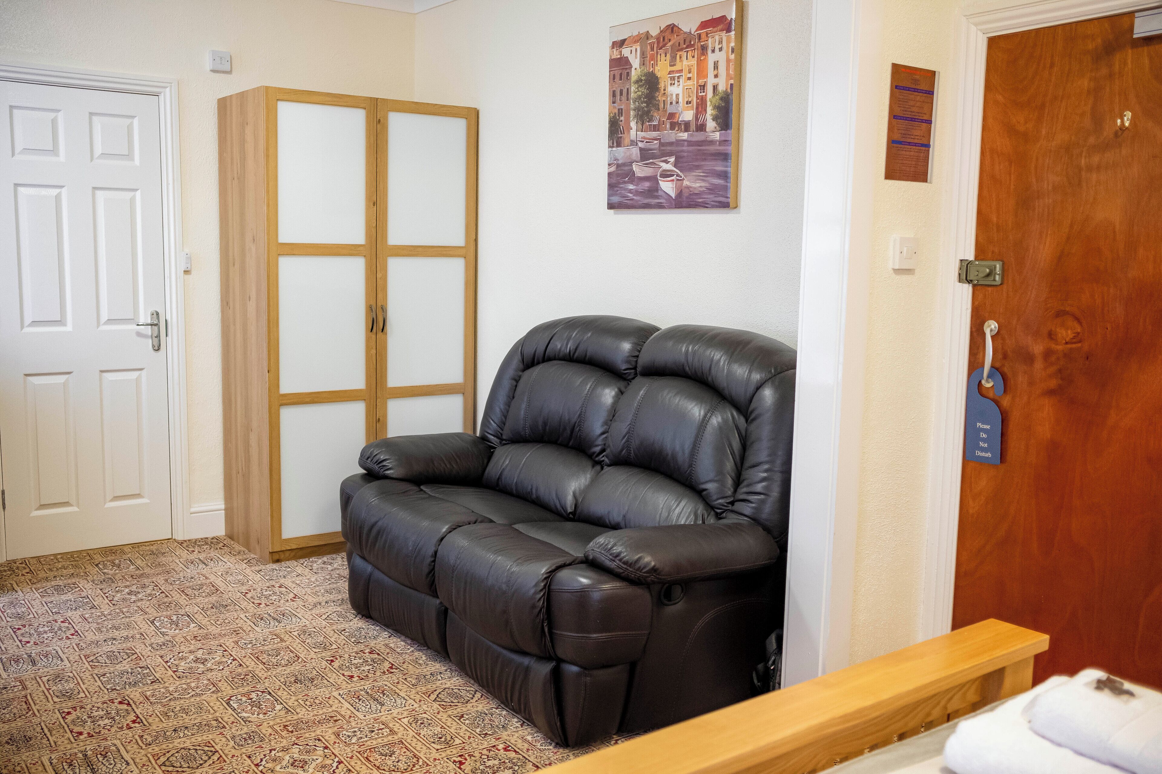 Una habitación con un sofá de cuero marrón, un armario de madera y una puerta con manija.