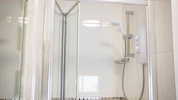 Ducha envuelta en vidrio con cabezal de ducha de mano y panel de control en la pared.