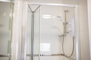Ducha envuelta en vidrio con cabezal de ducha de mano y panel de control en la pared.