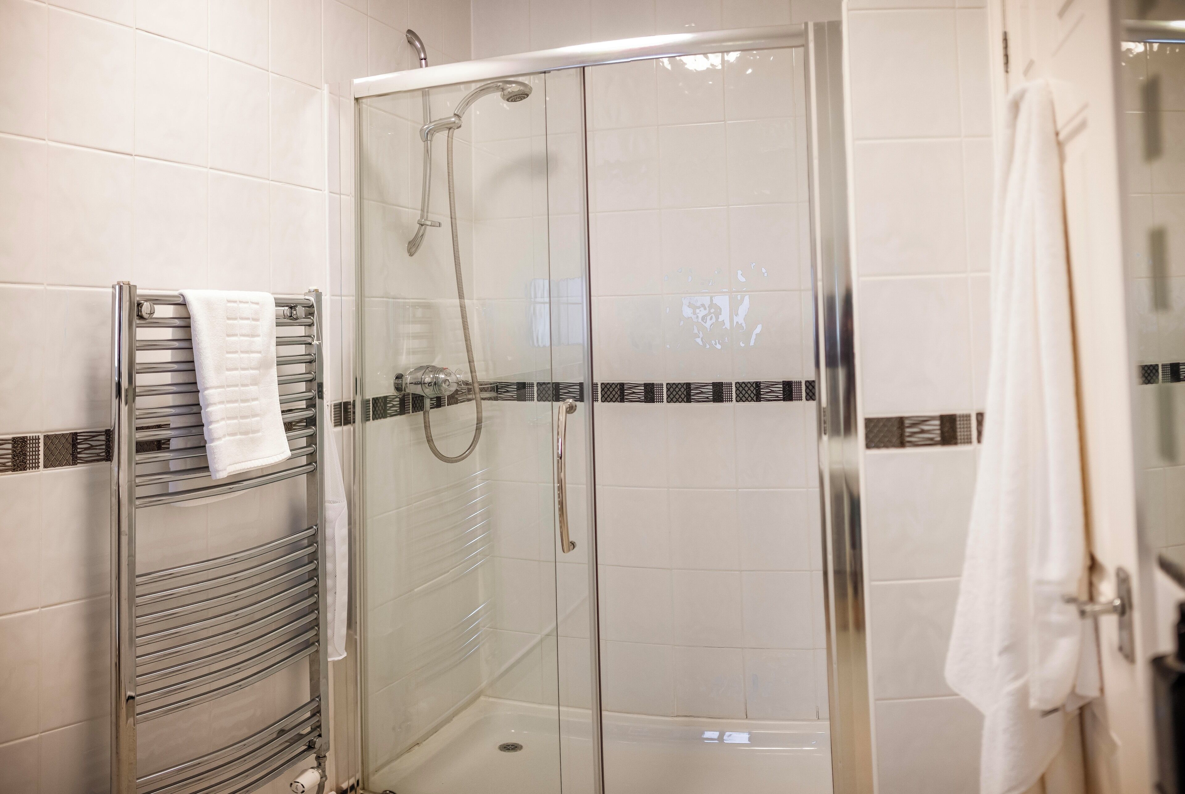 Een douche met glazen wanden, een chromen handdoekhouder en een witte handdoek aan de muur.