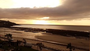 A coastal road with a beach and a distant view of the sea during sunset. - Opul Express (Douglas)