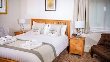 A neatly made bed with a wooden headboard, two bedside tables with lamps, a brown armchair, and a patterned carpet.