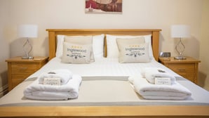 A neatly made double bed with two pillows labeled "Inglewood Guesthouse," two bedside lamps, and a folded towel on each side. - Opul Express (Douglas)