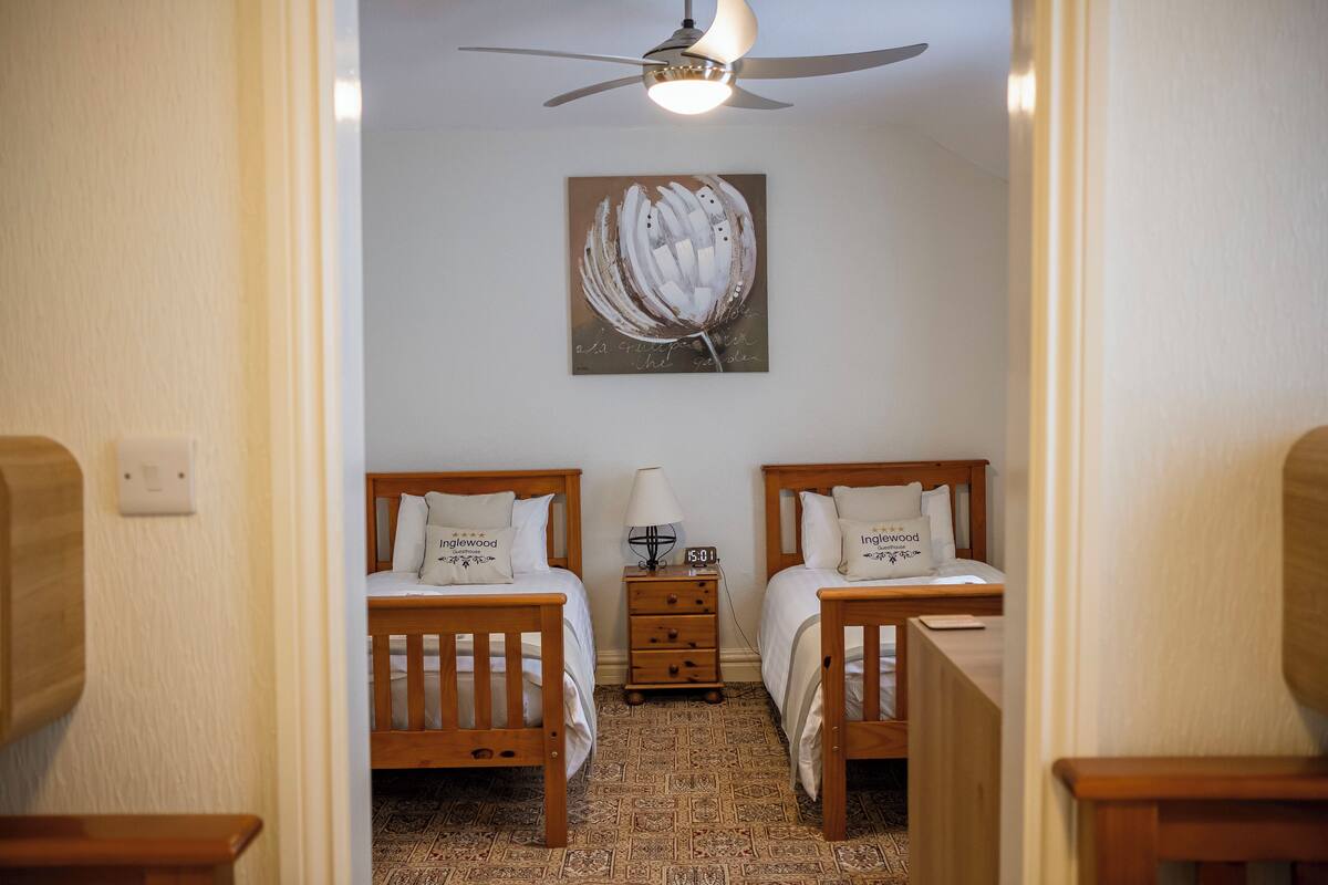 A hotel room with two wooden beds, a nightstand, a ceiling fan, and a wall-mounted artwork.
