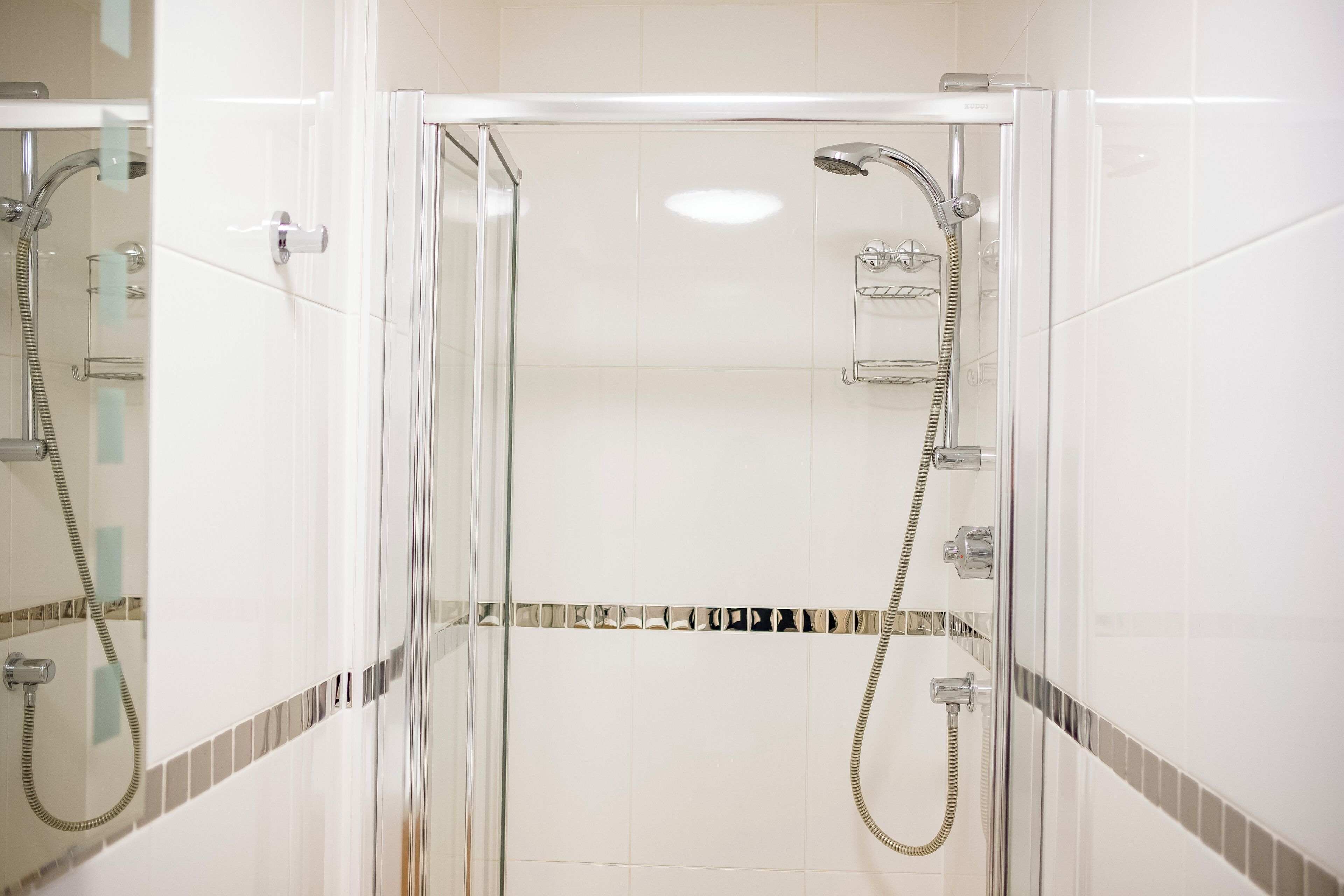 Un box de ducha con paredes de vidrio, un cabezal de ducha manual y un grifo instalado en la pared.