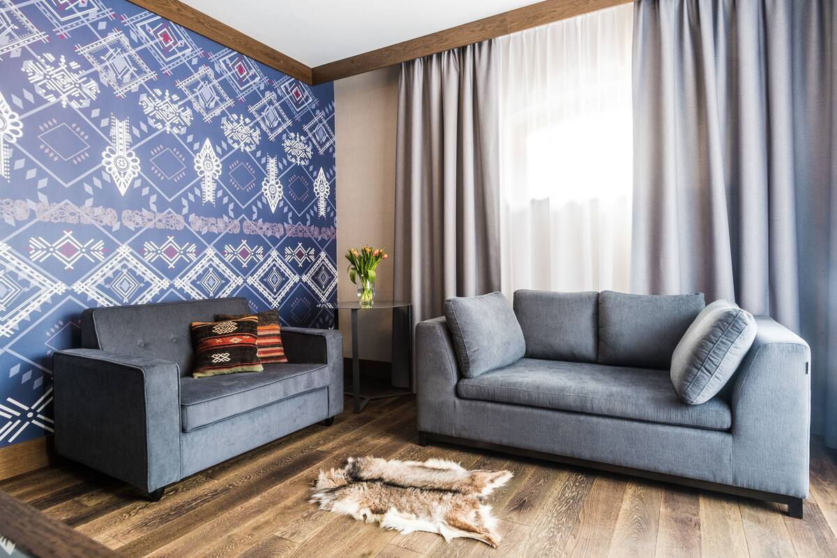 Een woonkamer met twee grijze banken, een behang met patroon, een houten vloer en een vachtkleed.