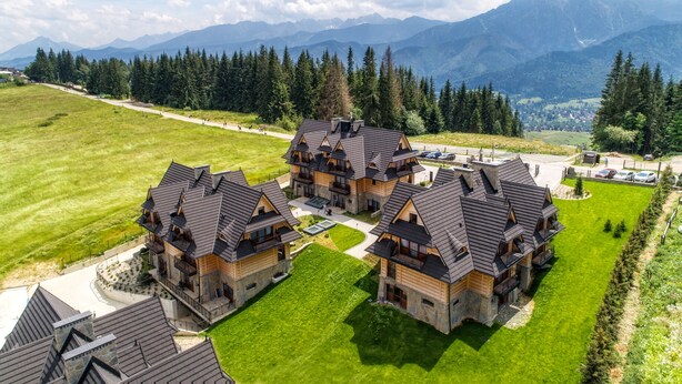 A cluster of wooden buildings with sloped roofs, surrounded by a well-maintained lawn and a forested area.