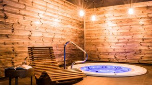 A wooden sauna with a hot tub, benches, and a reading area.