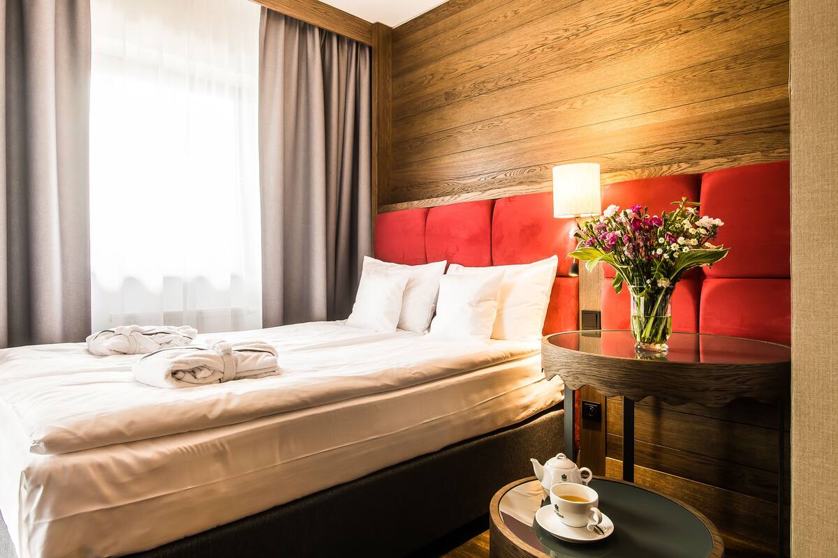 Een hotelkamer met een bed, een nachtkastje met een lamp, een bloevas en een kop thee.