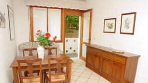 A dining area with a wooden table and chairs, a vase with flowers, and a wooden cabinet. - Lignano Pineta near Beach (Lignano Sabbiadoro)