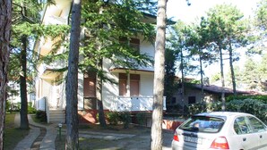 A residential building with a white facade, a balcony, and a parked car. - Lignano Pineta near Beach (Lignano Sabbiadoro)