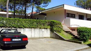 Um carro conversível preto estacionado em uma entrada de garagem, com um edifício branco ao fundo.