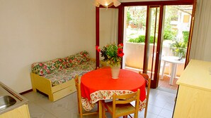 Uma cozinha compacta com uma mesa de jantar e cadeiras, um sofá e uma pequena mesa com um vaso de flores.