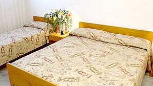 Um quarto com duas camas, uma mesinha com um vaso de flores e uma janela com cortinas.