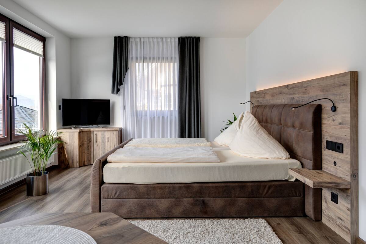Een slaapkamer met een bed, een televisie, een plant en een raam met gordijnen.