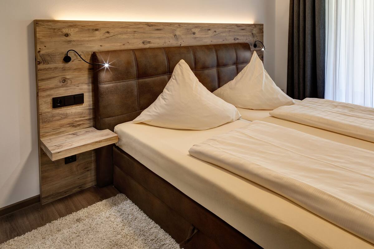 Een slaapkamer met een houten hoofdbord, twee kussens, een nachtkastje en een witte dekbedovertrek.